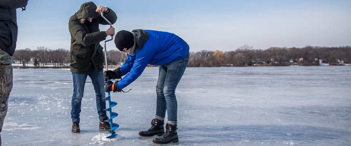 two people drilling a hole in the ice on a lake.