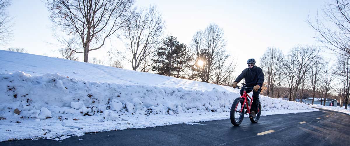 A person bikes down a paved trail in the winter.