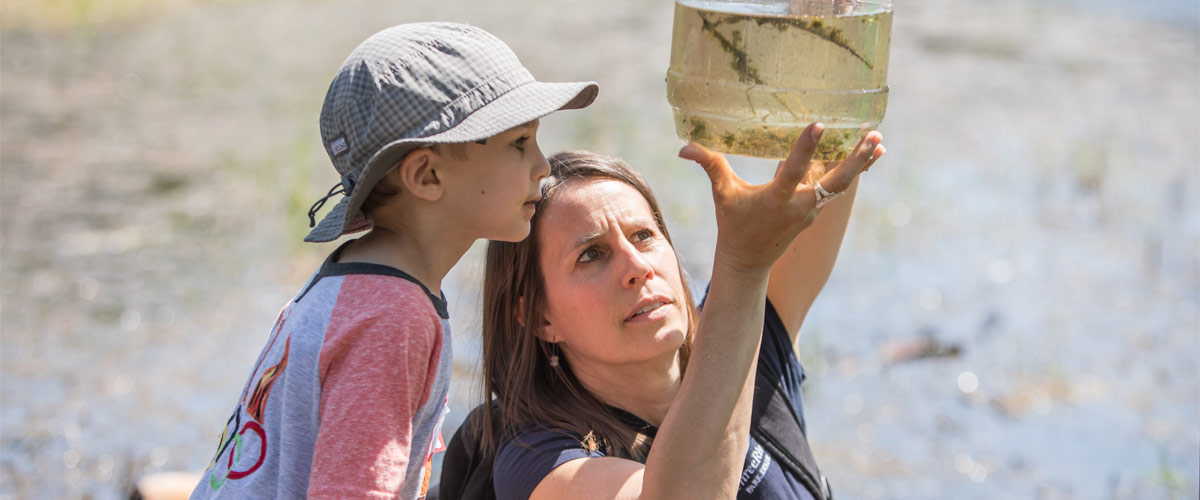 A naturalist shows a boy a jar of pond water.