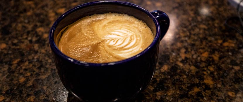 Latte art decorates the surface of a latte in a dark blue mug.