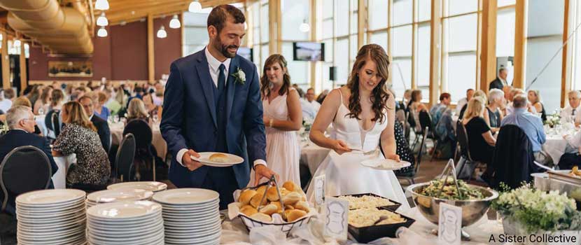 A photo of a bride and groom getting food from a table.