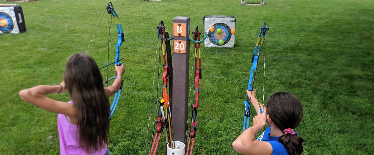 Two girls shoot bows on an archery range.