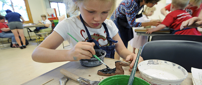 a young girl paints a piece of pottery