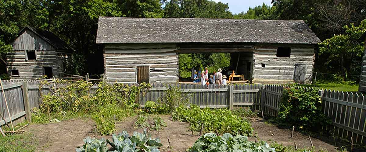 an old cabin stands beside a garden 