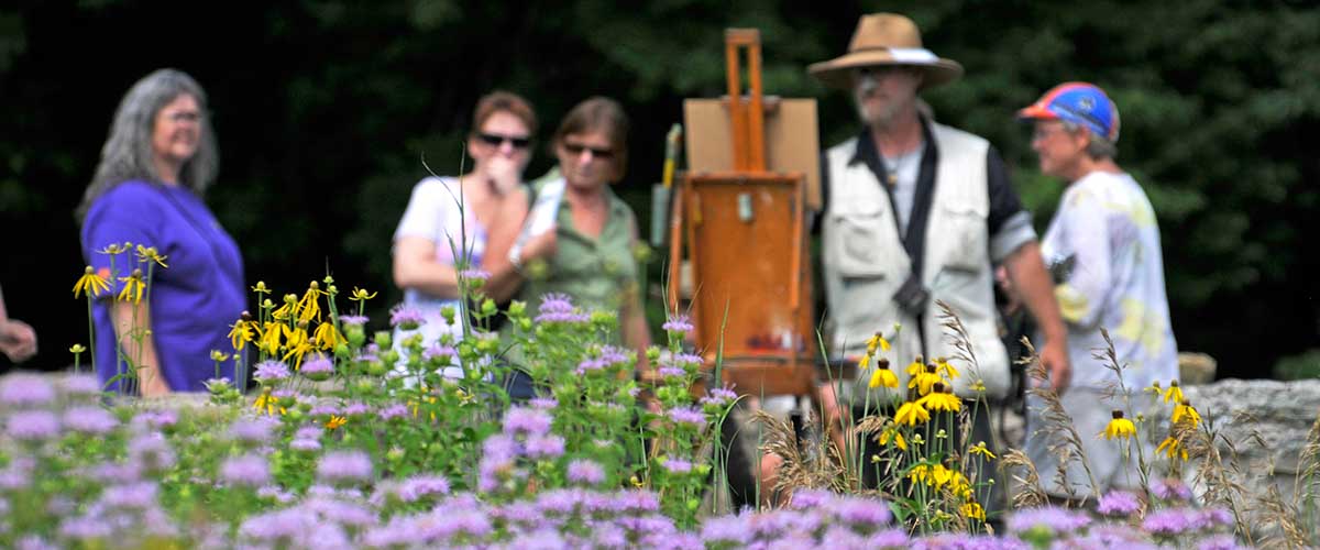 Group of women observe painter behind flowers