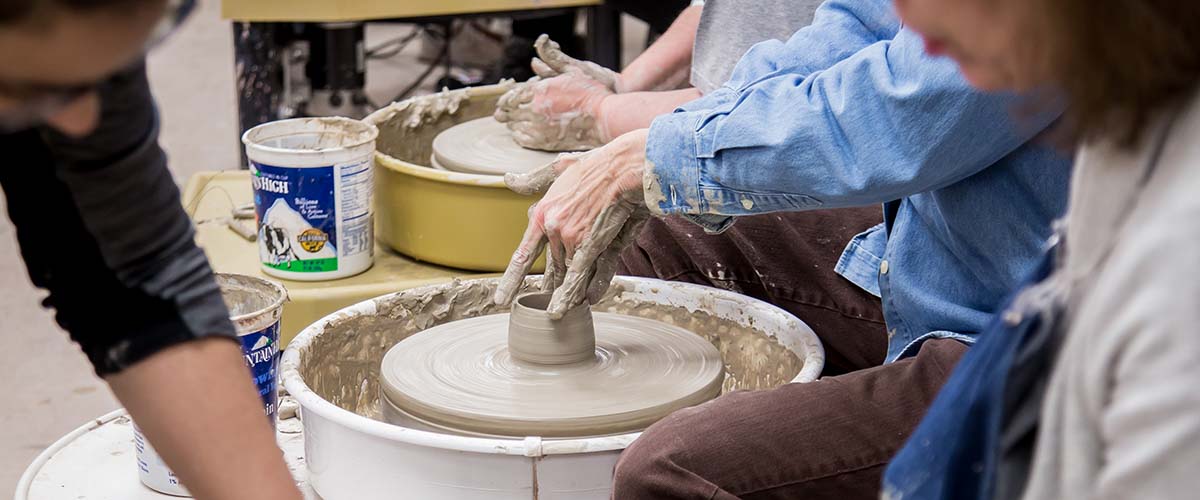 Student forming clay bowl on potters wheel