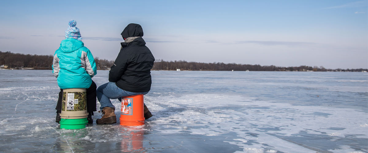two people sitting on buckets ice fishing