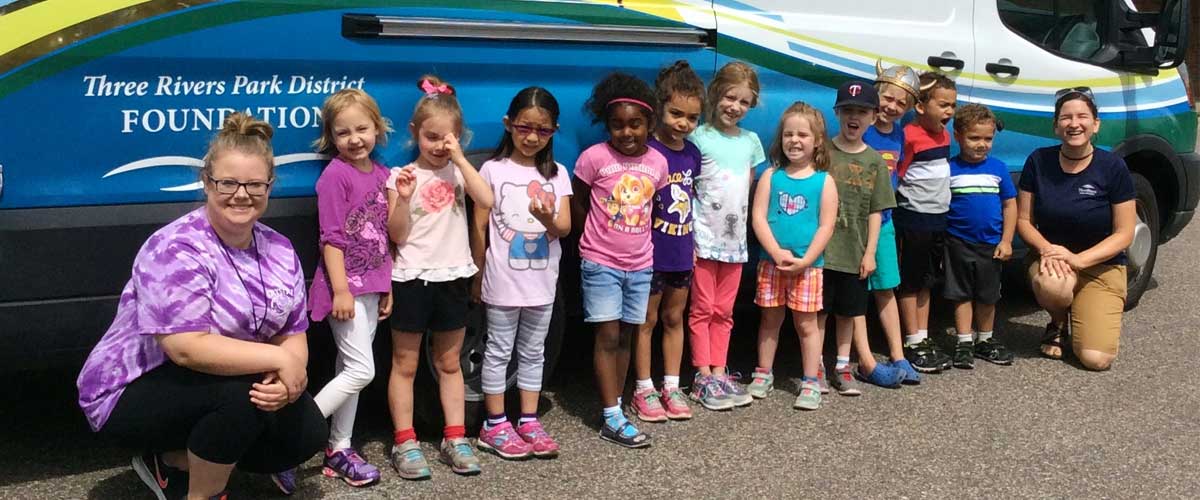children and camp leaders standing in front of a van that says Three Rivers Park District Foundation.