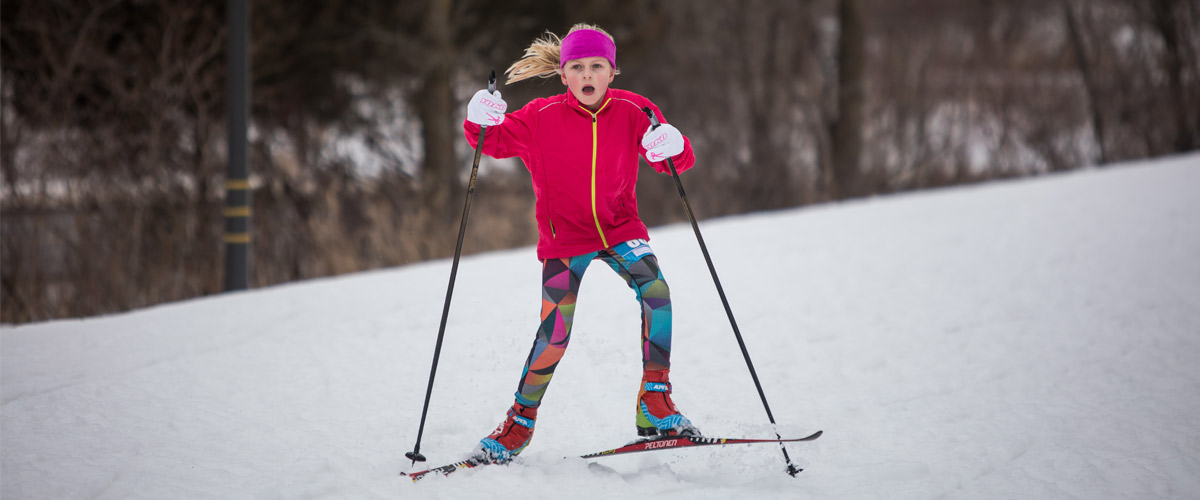 a blonde girl in a pink coat cross-country skiing. 
