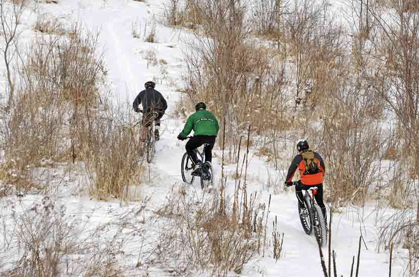 three mountain bikers on a snowy trail.