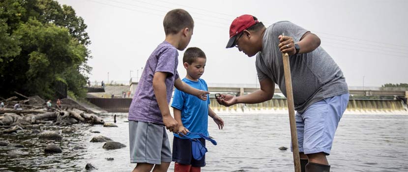 a dad shows his sons something he found while wading in a river.