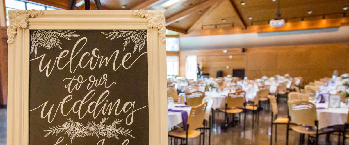 a chalkboard sign says "welcome to our wedding." in the background there are table set for dinner.