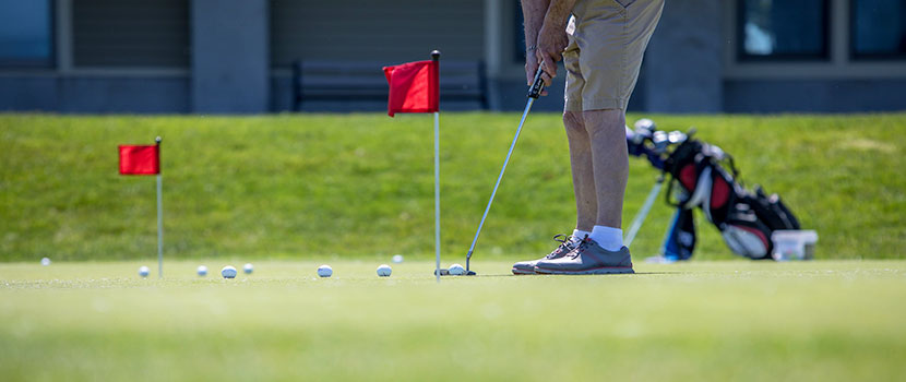 the legs of a person setting up to putt on a practice putting green.