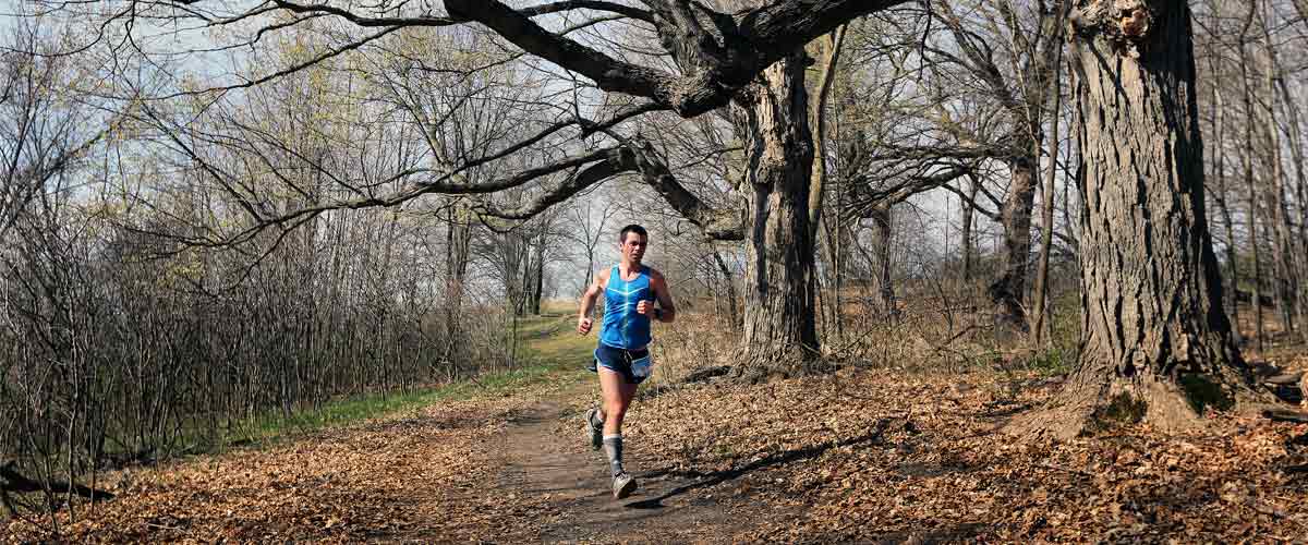 a man running on a trail through the woods in the spring.