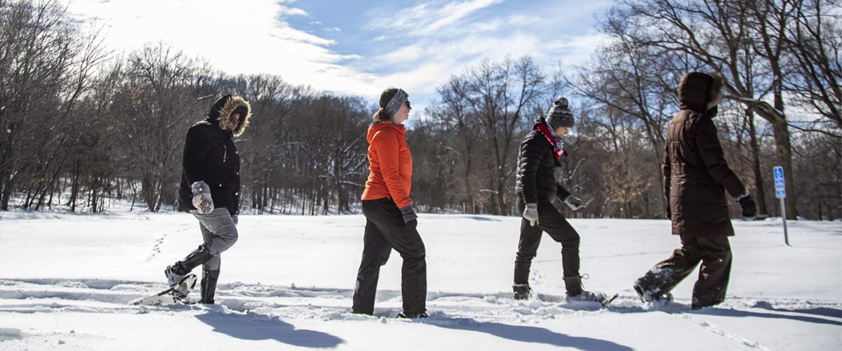 four people snowshoeing through a snowy park