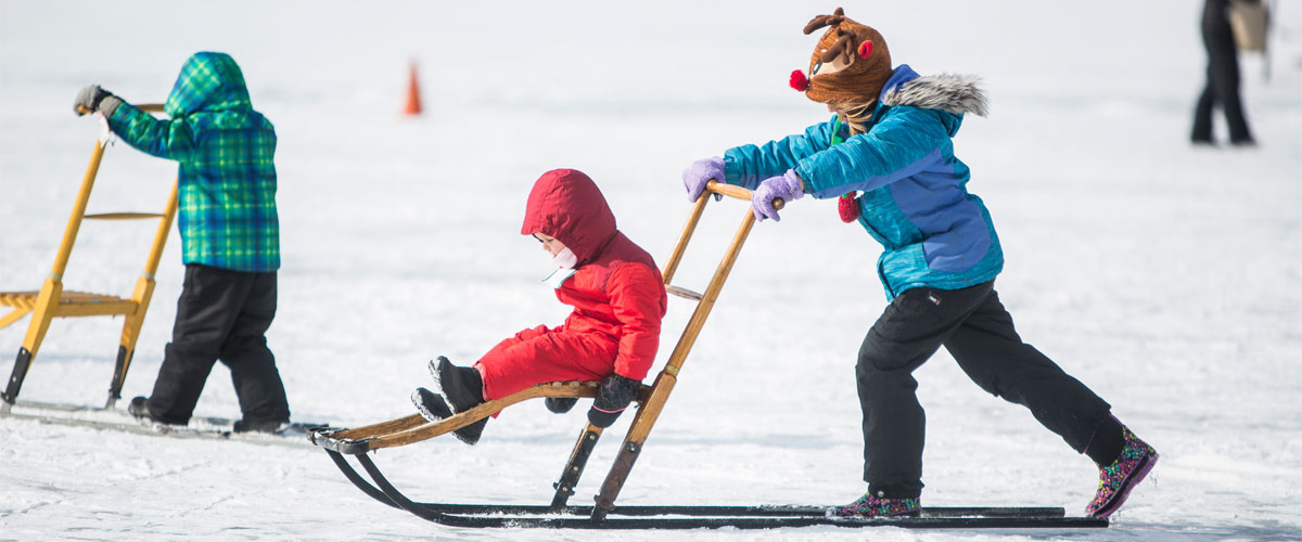 Kids push each other across a frozen lake on kicksleds.