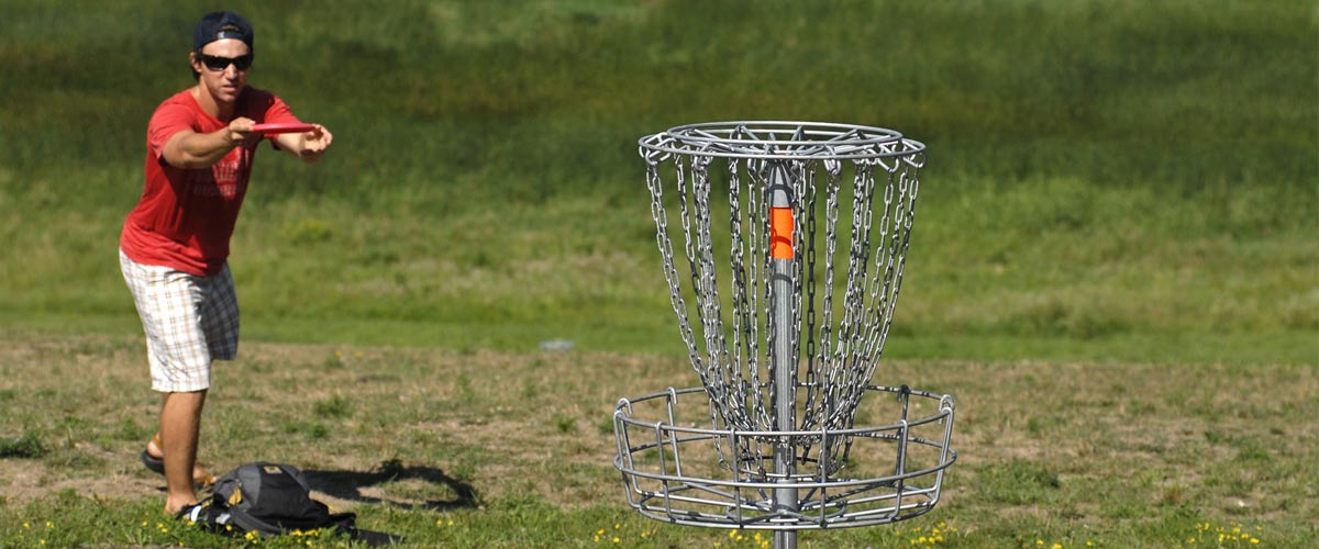 a man throws a disc toward a goal on a disc golf course.