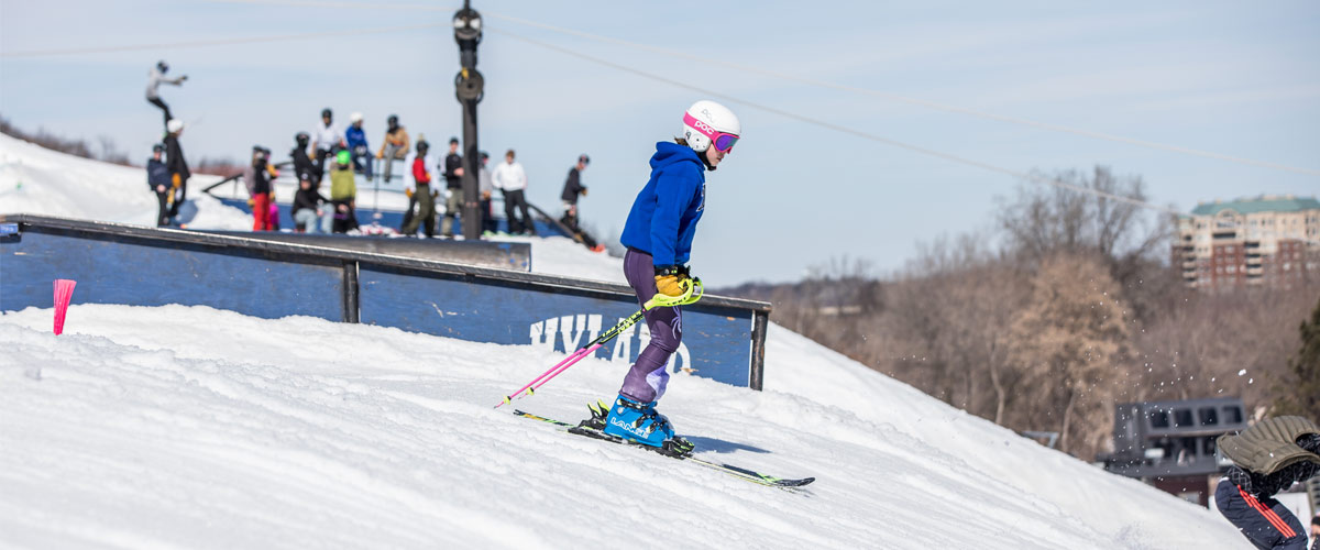 a girl goes down a ski hill wearing a helmet and a blue coat.