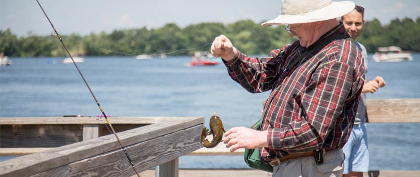 An older man reaches for a fish he caught from a wooden pier.