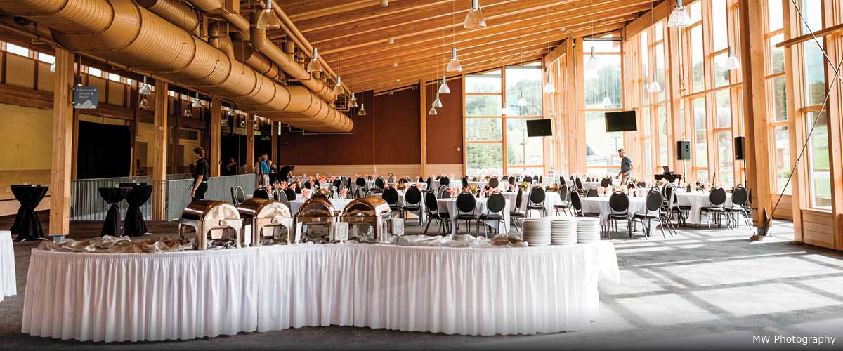 The inside of a banquet hall set for a wedding. The room has high ceilings and tall windows on one wall.