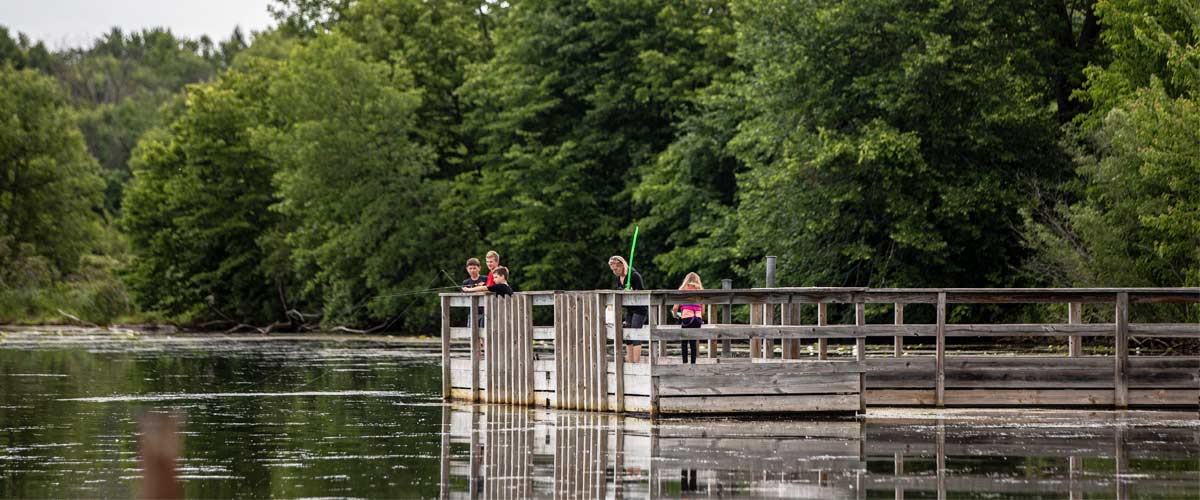 People fishing off a wooden pier on a lake.