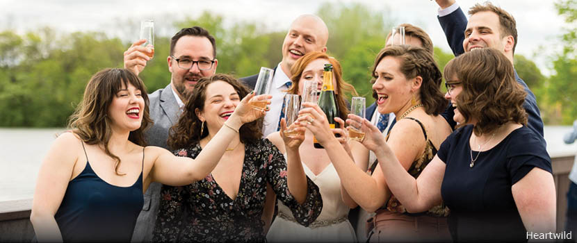 A bridal party holds up glasses of champagne on a bridge outdoors.