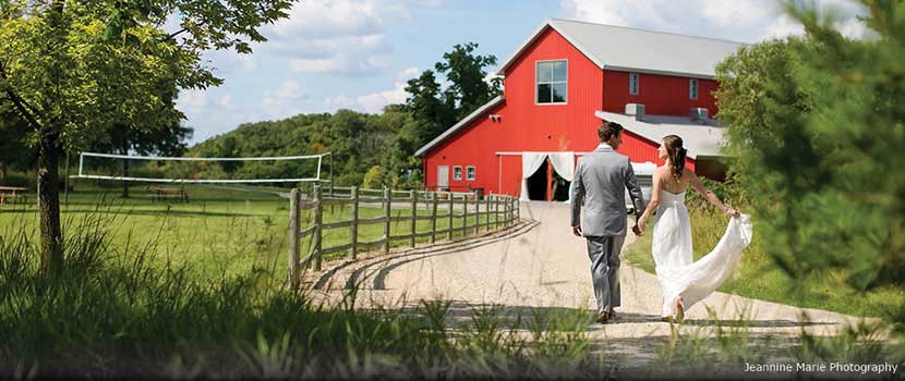 A bride and groom walk toward a red barn.