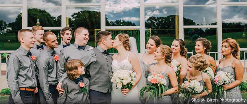 A wedding party watches as the bride and groom kiss.