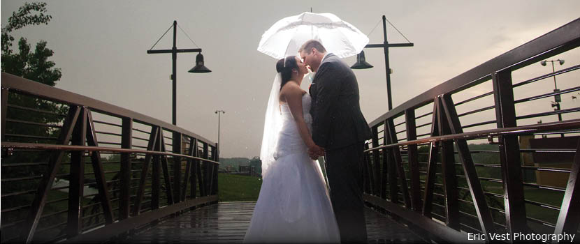 A bride and groom kiss under an umbrella on a bridge.