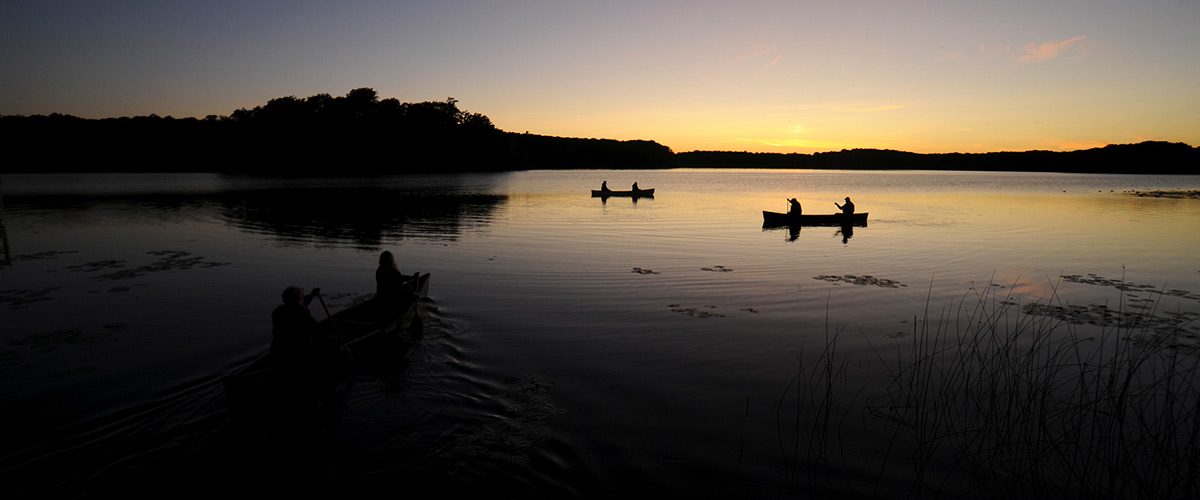 three canoes paddling on a lake just after sunset