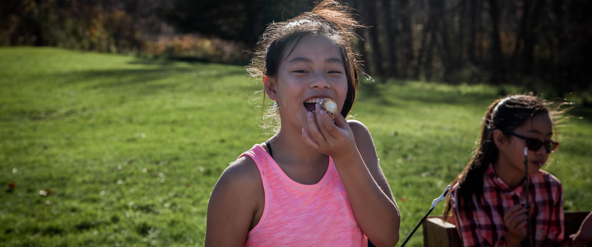 A girl smiles as she eats a roasted marshmallow in the summer.