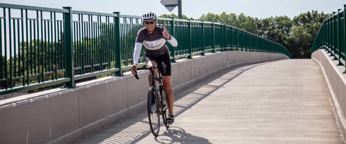 A man smiles as he bikes over a concrete bridge.