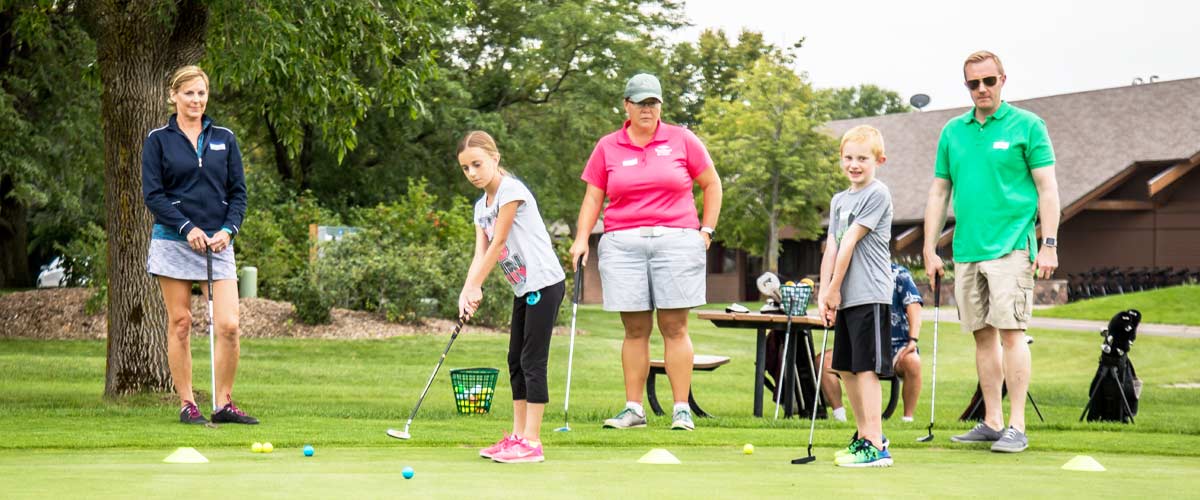A woman leads a golf lesson of adults and children.