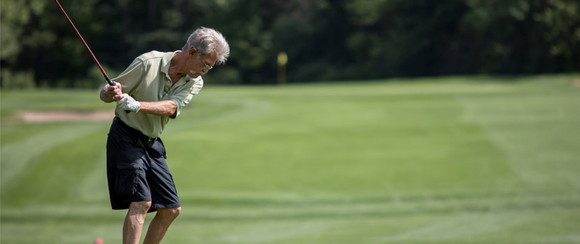 An older man swings a golf club.
