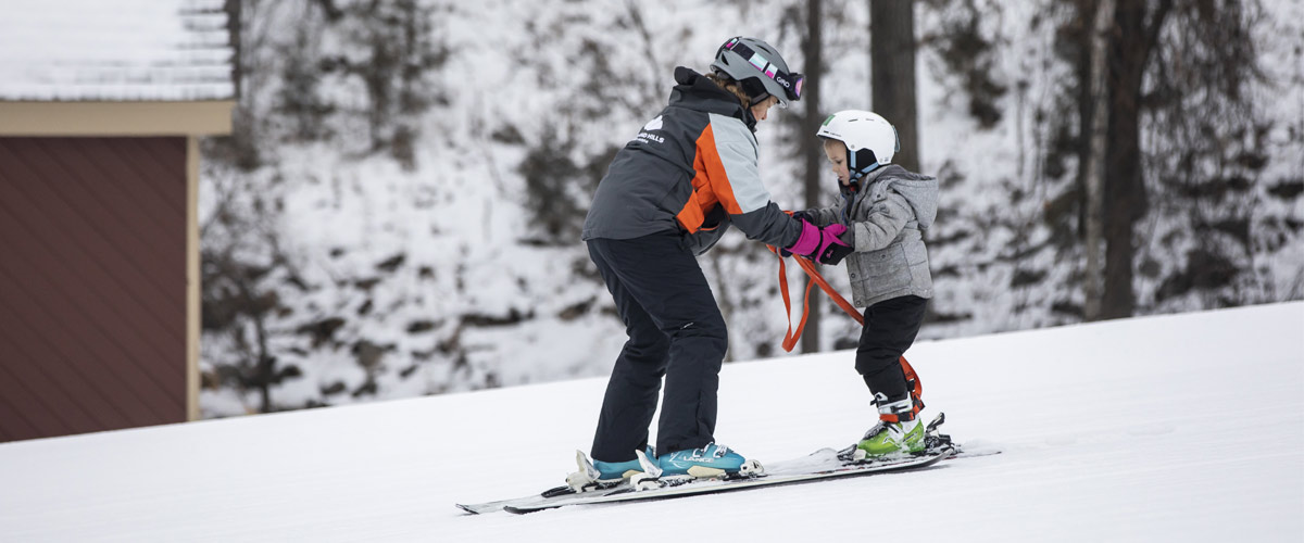 An instructor teaches a boy how to downhill ski.