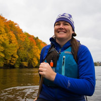 A woman smiles while paddling a canoe in the fall.