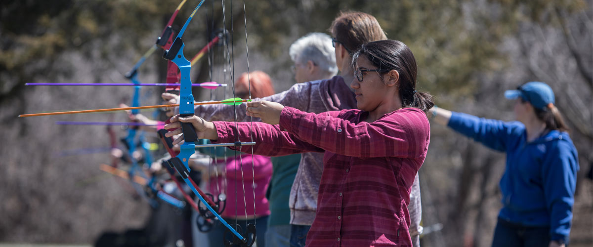 A woman aims a bow and arrow in an archery program.
