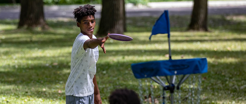 A boy throws a disc toward a goal in a game of disc golf.