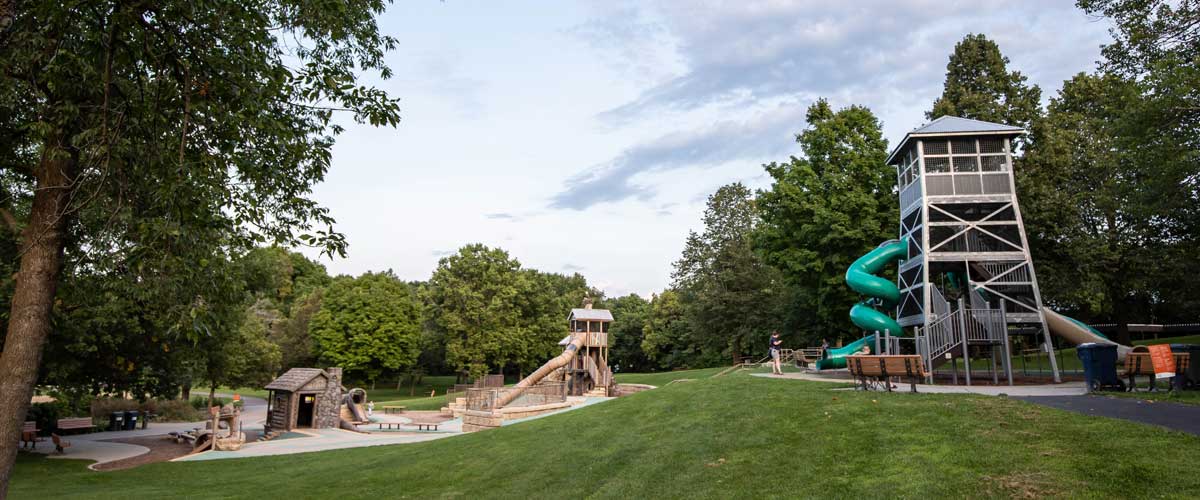 A play area with towers and slides sits in a clearing surrounded by trees.