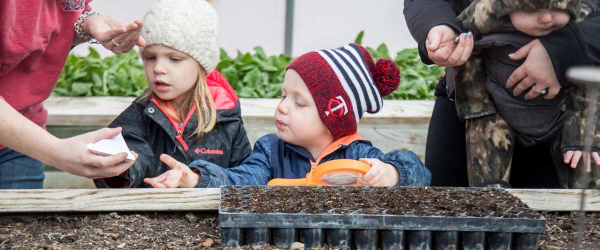 Two kids look at seedlings in a greenhouse.