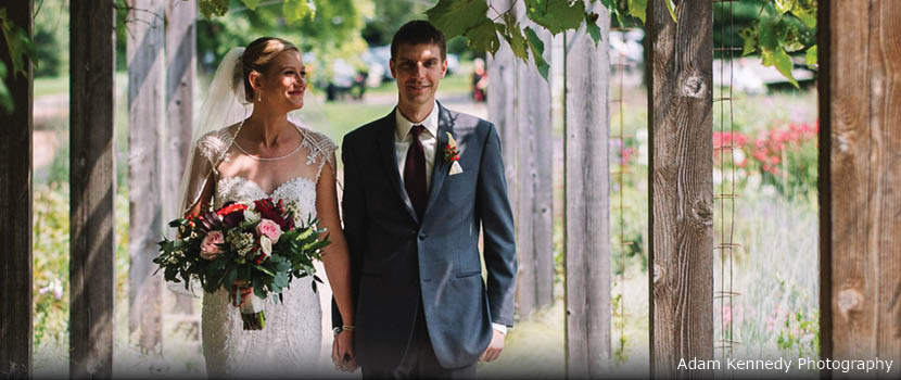 A bride and groom walk down a covered walkway in a garden.
