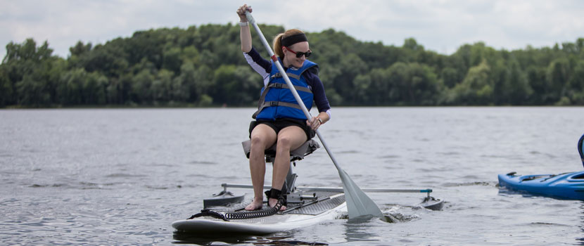 A woman paddles an adapted paddleboard on a lake.