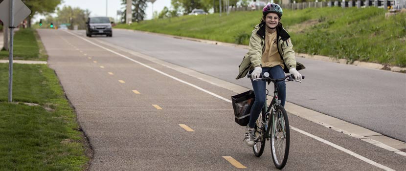 A girl smiles as she bikes down a paved bike path.