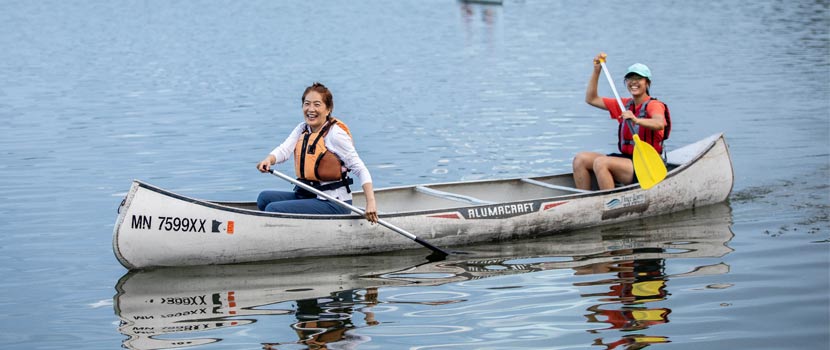 Two women paddle a canoe on a lake.