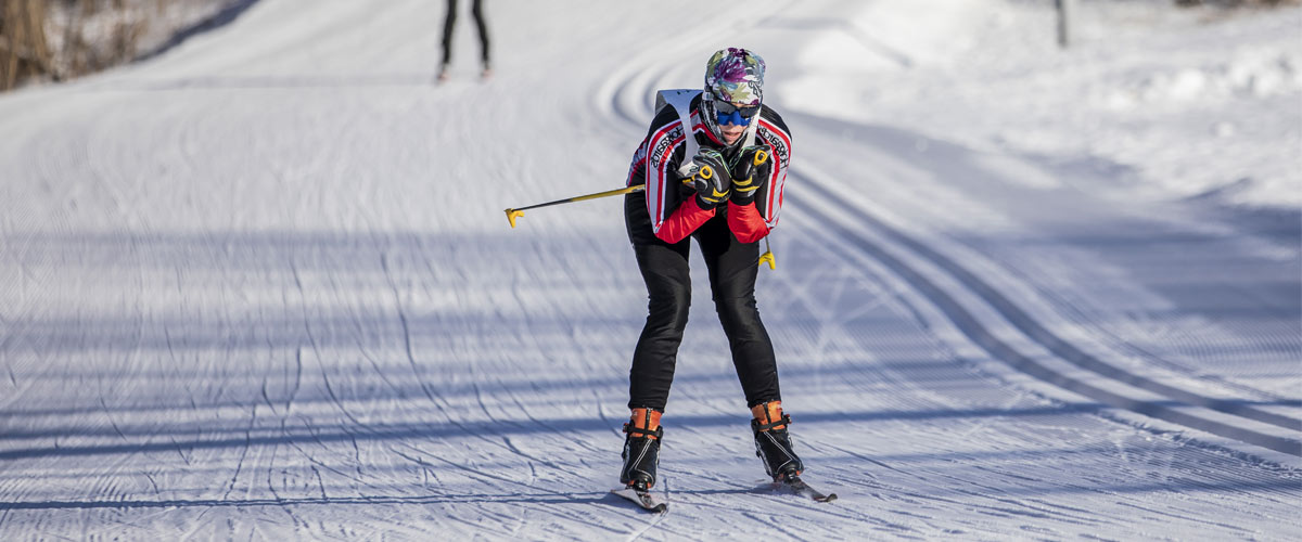 A woman crouches down as she coasts down a snowy trail in a cross-country ski race.