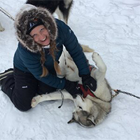 profile picture of mari in a winter coat petting a shepherd dog in the snow