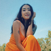 Kaja Vang wears and orange dress while posing for a photos outdoors.