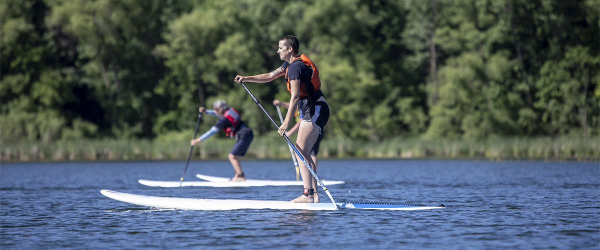 Two people paddle stand-up paddleboards on a lake.