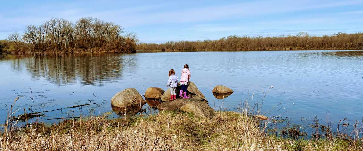 Two girls stand on the edge of a lake in the spring.