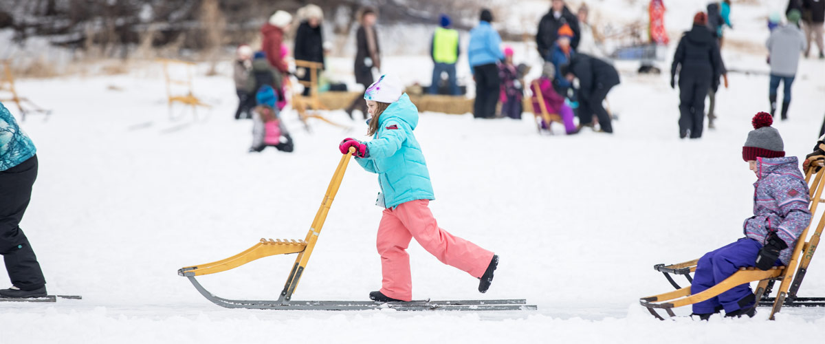 A girl uses a kicksled on a snowy landscape.